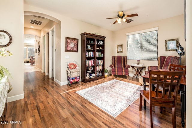 living area featuring arched walkways, wood finished floors, visible vents, and baseboards