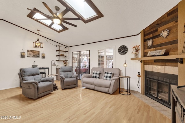 living room featuring a tile fireplace, crown molding, vaulted ceiling with skylight, and light hardwood / wood-style floors