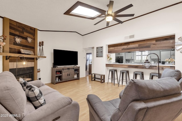 living room featuring light hardwood / wood-style flooring, ceiling fan, a fireplace, ornamental molding, and vaulted ceiling