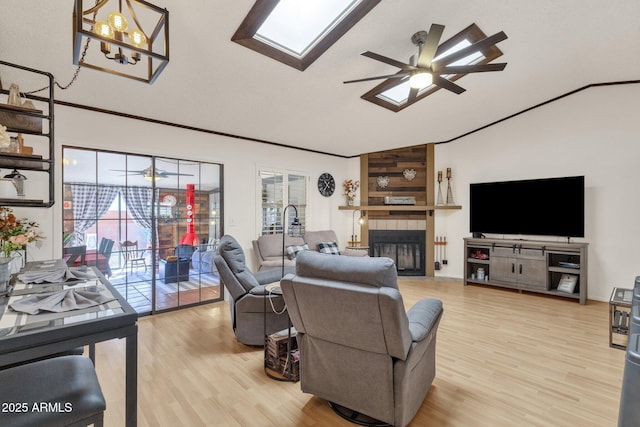 living room with ceiling fan, lofted ceiling with skylight, and a tile fireplace