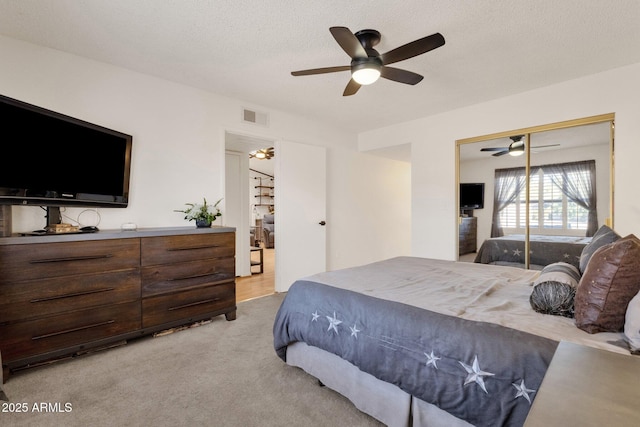 bedroom featuring ceiling fan, a closet, light carpet, and a textured ceiling