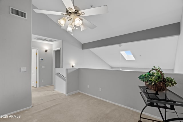 unfurnished room with vaulted ceiling, a skylight, a ceiling fan, carpet floors, and an upstairs landing
