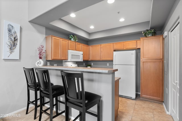kitchen with white appliances, a peninsula, a kitchen bar, a tray ceiling, and light countertops