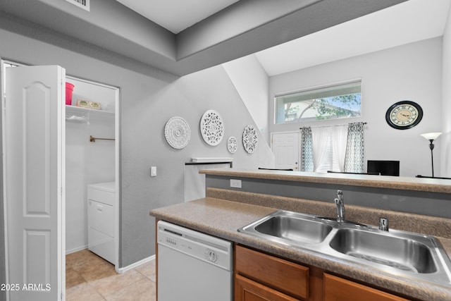 kitchen with white dishwasher, a sink, brown cabinetry, washer / clothes dryer, and light tile patterned floors
