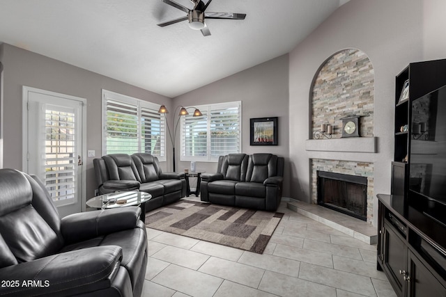 tiled living room featuring ceiling fan, vaulted ceiling, and a stone fireplace