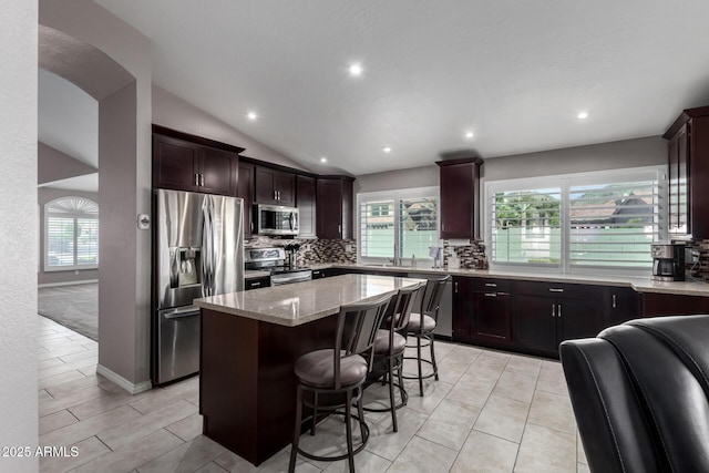 kitchen featuring light stone counters, vaulted ceiling, stainless steel appliances, a kitchen island, and plenty of natural light