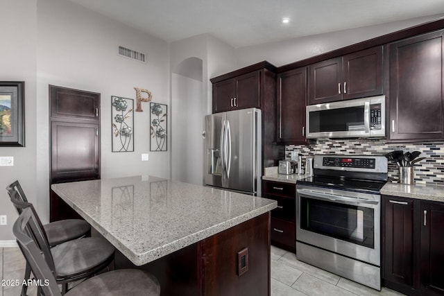 kitchen with vaulted ceiling, light stone counters, a breakfast bar area, a kitchen island, and appliances with stainless steel finishes