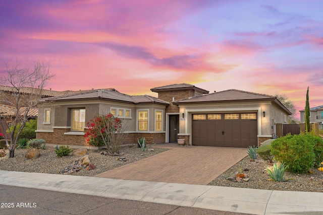 prairie-style home featuring decorative driveway, fence, an attached garage, and stucco siding