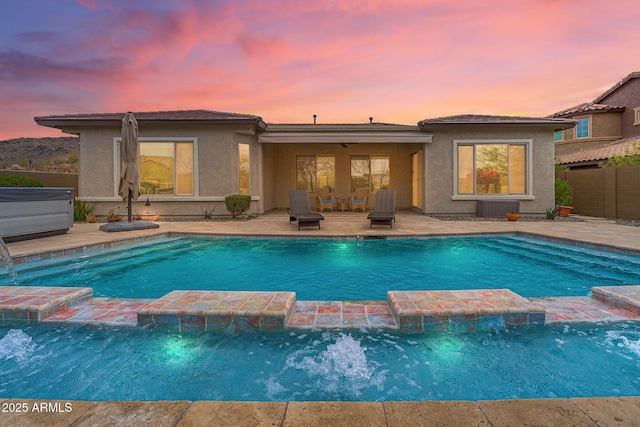 pool at dusk with a patio area, fence, and a pool with connected hot tub