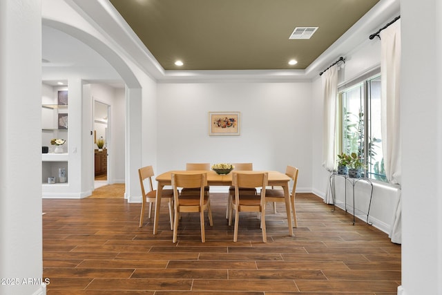 dining room featuring arched walkways, dark wood-type flooring, visible vents, baseboards, and a tray ceiling