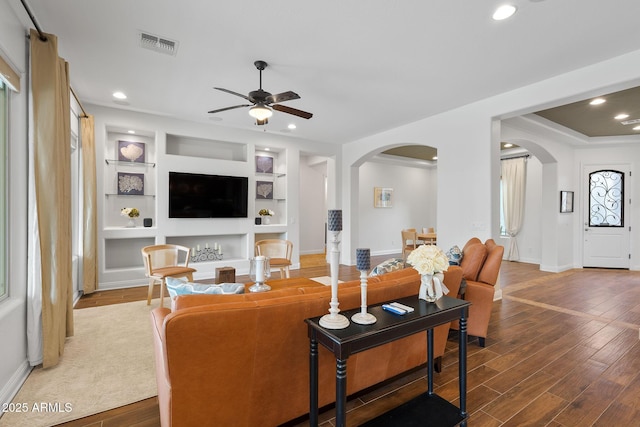 living room with arched walkways, wood finished floors, visible vents, and recessed lighting