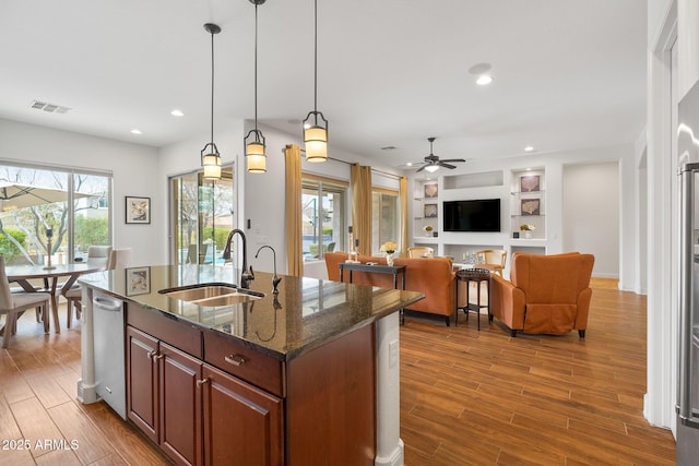 kitchen featuring wood finished floors, a sink, visible vents, dark stone countertops, and decorative light fixtures