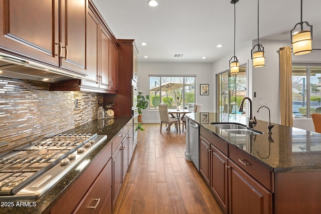 kitchen with tasteful backsplash, dark wood-style floors, dark stone countertops, stainless steel appliances, and a sink