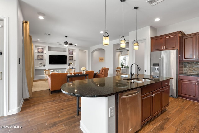 kitchen featuring arched walkways, appliances with stainless steel finishes, open floor plan, wood finish floors, and a sink