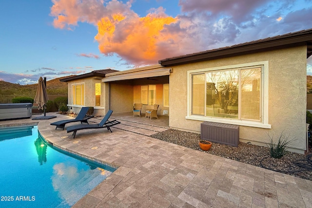 back of house at dusk featuring a patio, a hot tub, a fenced in pool, and stucco siding