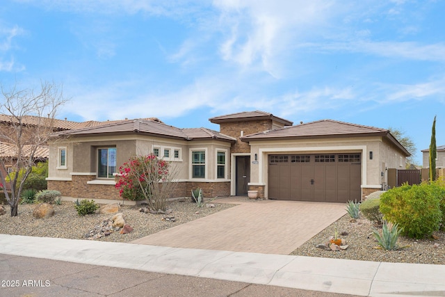 prairie-style house with decorative driveway, brick siding, an attached garage, and stucco siding