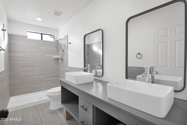 bathroom with a tile shower, vanity, a textured ceiling, and toilet