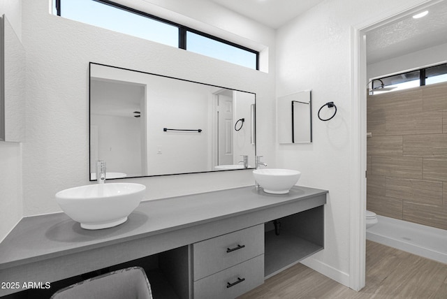 bathroom featuring a tile shower, hardwood / wood-style floors, vanity, and toilet