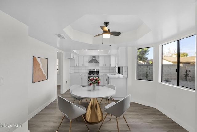 dining area featuring a tray ceiling, ceiling fan, dark wood-type flooring, and sink