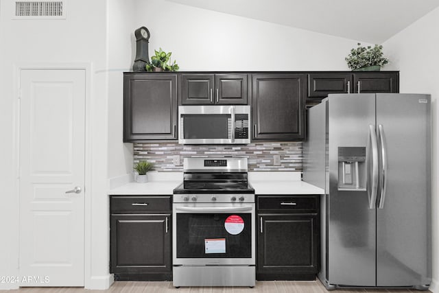 kitchen featuring light wood-type flooring, appliances with stainless steel finishes, backsplash, and lofted ceiling