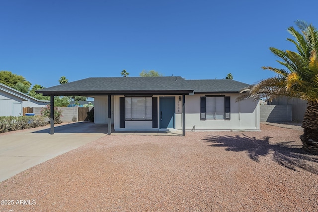 ranch-style home with driveway, fence, a carport, and roof with shingles