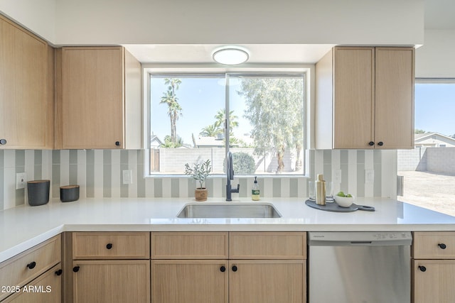 kitchen featuring stainless steel dishwasher, a sink, light countertops, and backsplash