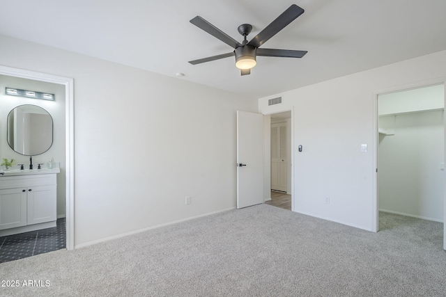 unfurnished bedroom with carpet flooring, a spacious closet, connected bathroom, and baseboards