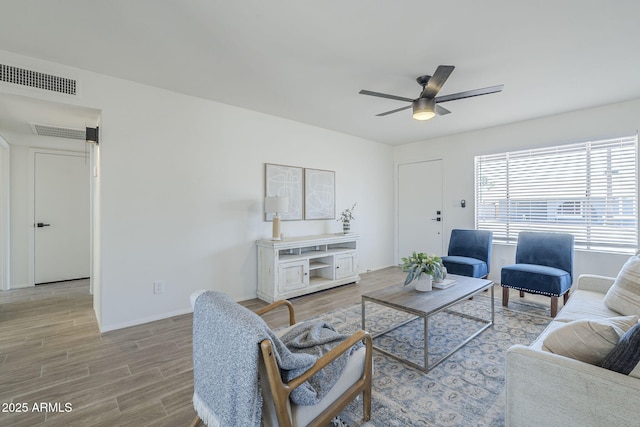 living area with light wood finished floors, a ceiling fan, and baseboards