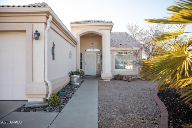 view of exterior entry with a tiled roof, an attached garage, and stucco siding