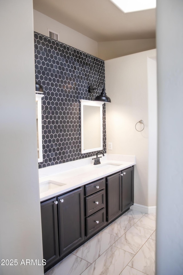 bathroom featuring marble finish floor, double vanity, a sink, and baseboards