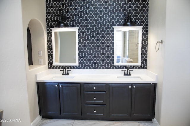 full bath featuring double vanity, marble finish floor, tasteful backsplash, and a sink