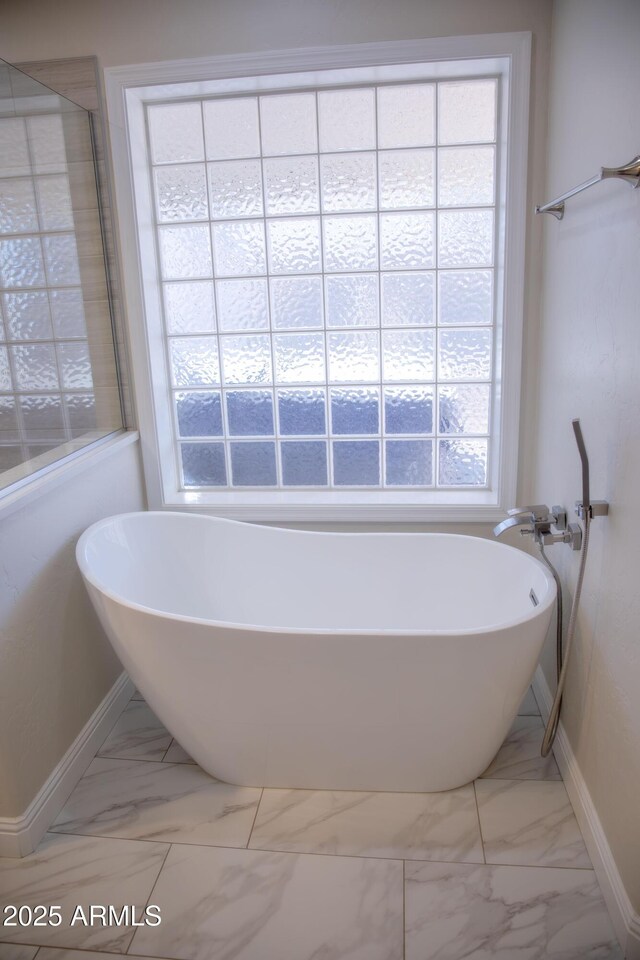 bathroom featuring marble finish floor, a soaking tub, and baseboards