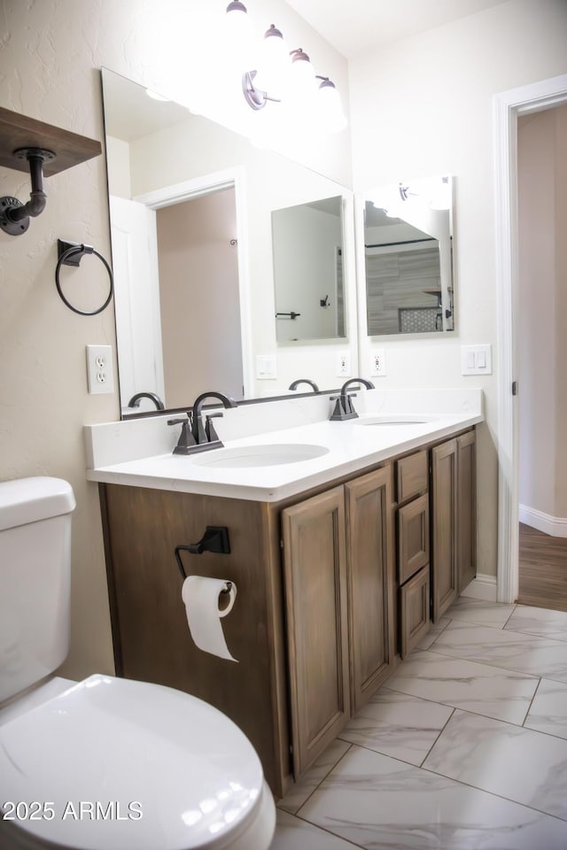 bathroom with marble finish floor, a sink, toilet, and double vanity