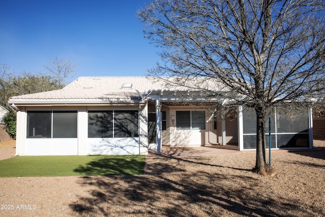 back of house featuring a sunroom, a tile roof, a lawn, and stucco siding