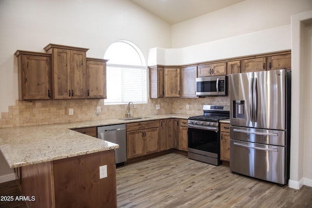 kitchen featuring light stone counters, a peninsula, a sink, appliances with stainless steel finishes, and light wood-type flooring