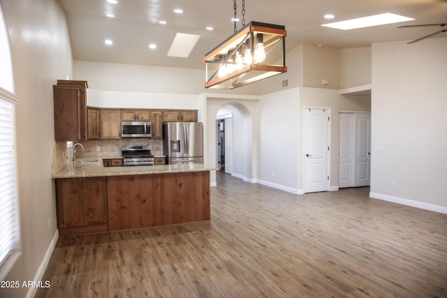 kitchen with a skylight, arched walkways, brown cabinets, stainless steel appliances, and a sink