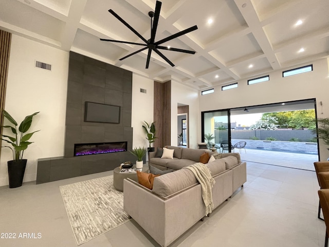 living room with beamed ceiling, ceiling fan, a towering ceiling, and a tiled fireplace