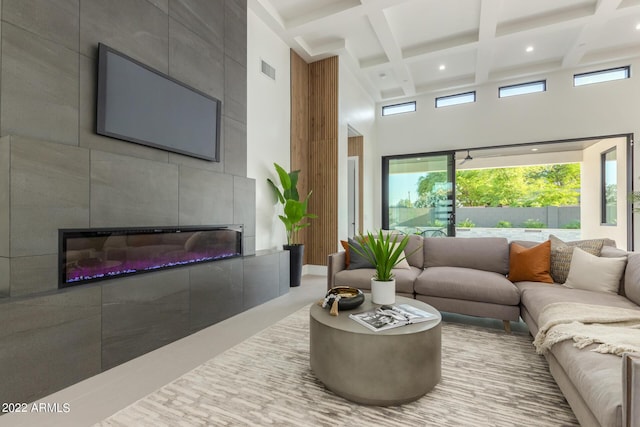 living room featuring beam ceiling, a high ceiling, a tile fireplace, and coffered ceiling