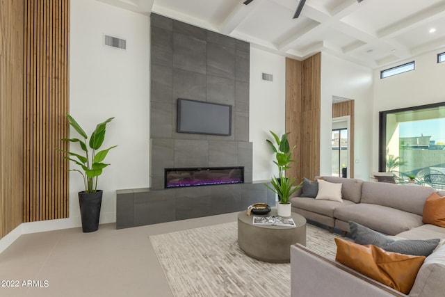 living room featuring beam ceiling, a high ceiling, a tile fireplace, and coffered ceiling