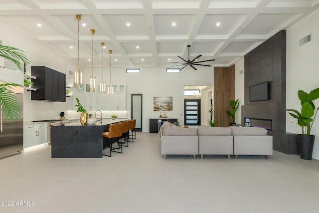 tiled living room featuring ceiling fan, beamed ceiling, and a high ceiling