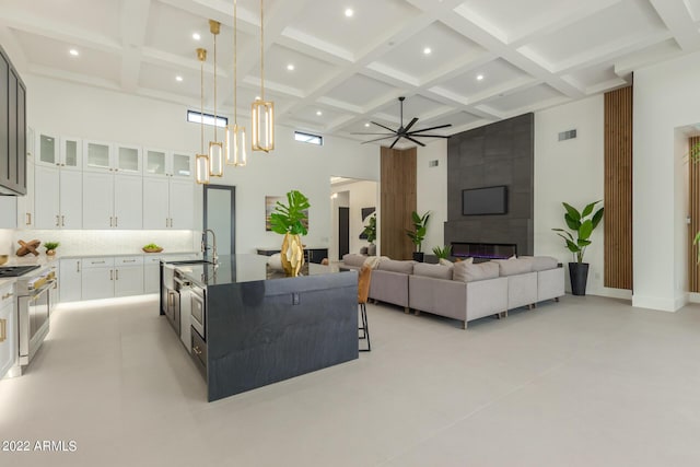 living room with ceiling fan, sink, beamed ceiling, a high ceiling, and a tiled fireplace