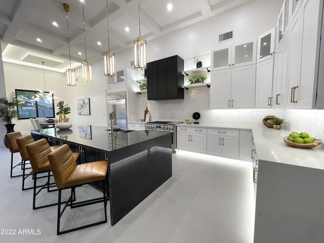 kitchen with high end range, tasteful backsplash, dark stone counters, a kitchen island with sink, and white cabinets