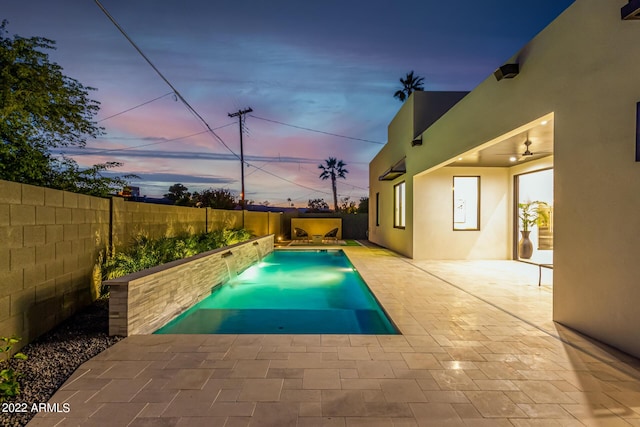 pool at dusk featuring pool water feature, ceiling fan, and a patio