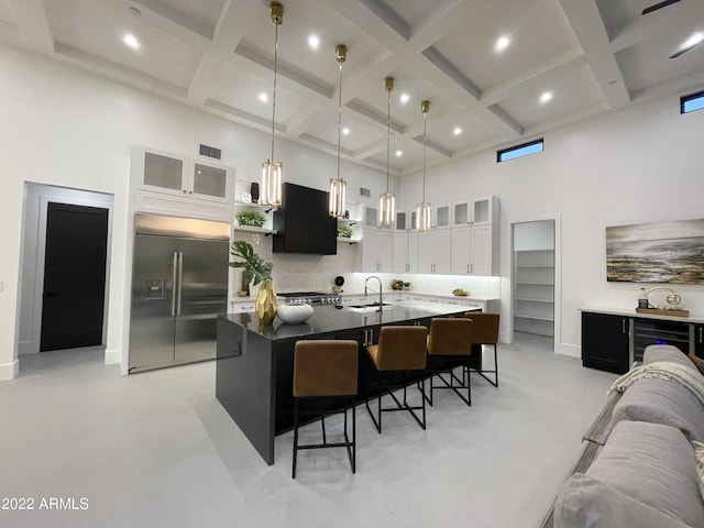 kitchen with a center island with sink, white cabinetry, stainless steel built in refrigerator, and a high ceiling