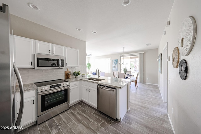 kitchen featuring white cabinets, appliances with stainless steel finishes, a peninsula, wood tiled floor, and a sink