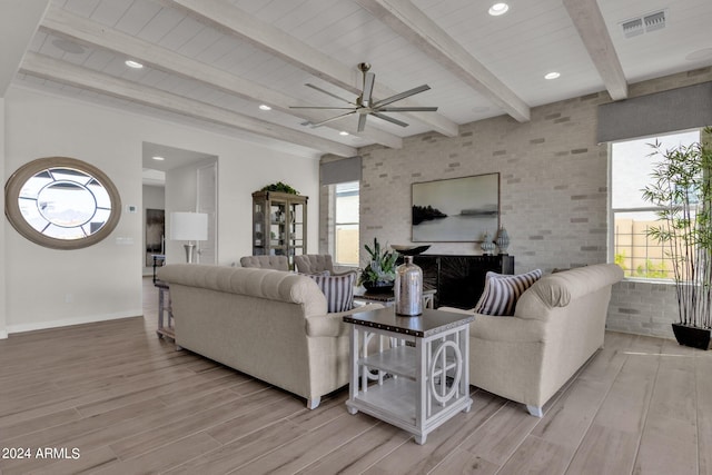 living room featuring ceiling fan, brick wall, plenty of natural light, and beamed ceiling