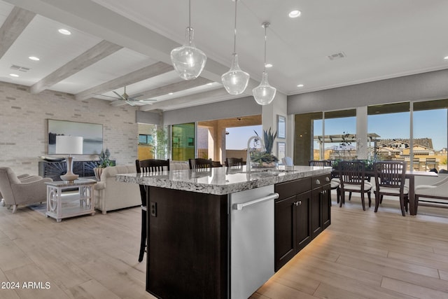 kitchen with a kitchen bar, a kitchen island with sink, light stone countertops, pendant lighting, and beam ceiling