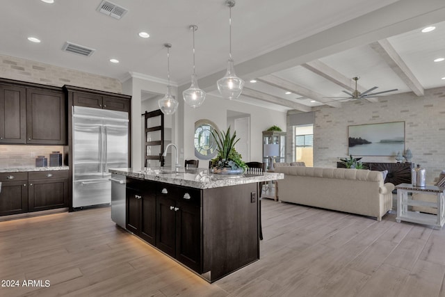 kitchen featuring pendant lighting, beam ceiling, dark brown cabinetry, appliances with stainless steel finishes, and an island with sink