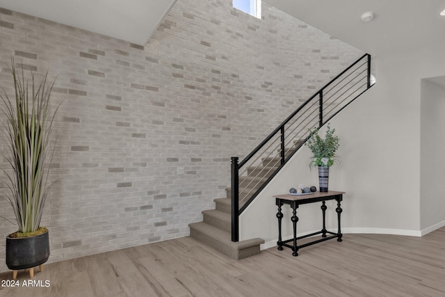 staircase featuring a towering ceiling, brick wall, and hardwood / wood-style flooring