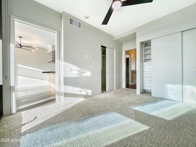 unfurnished bedroom with visible vents, two closets, ceiling fan, and carpet flooring